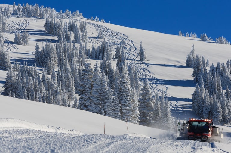 A snowcat drives down with ski tracks behind on a sunny powder day at Grand Targhee Resort, Wyoming