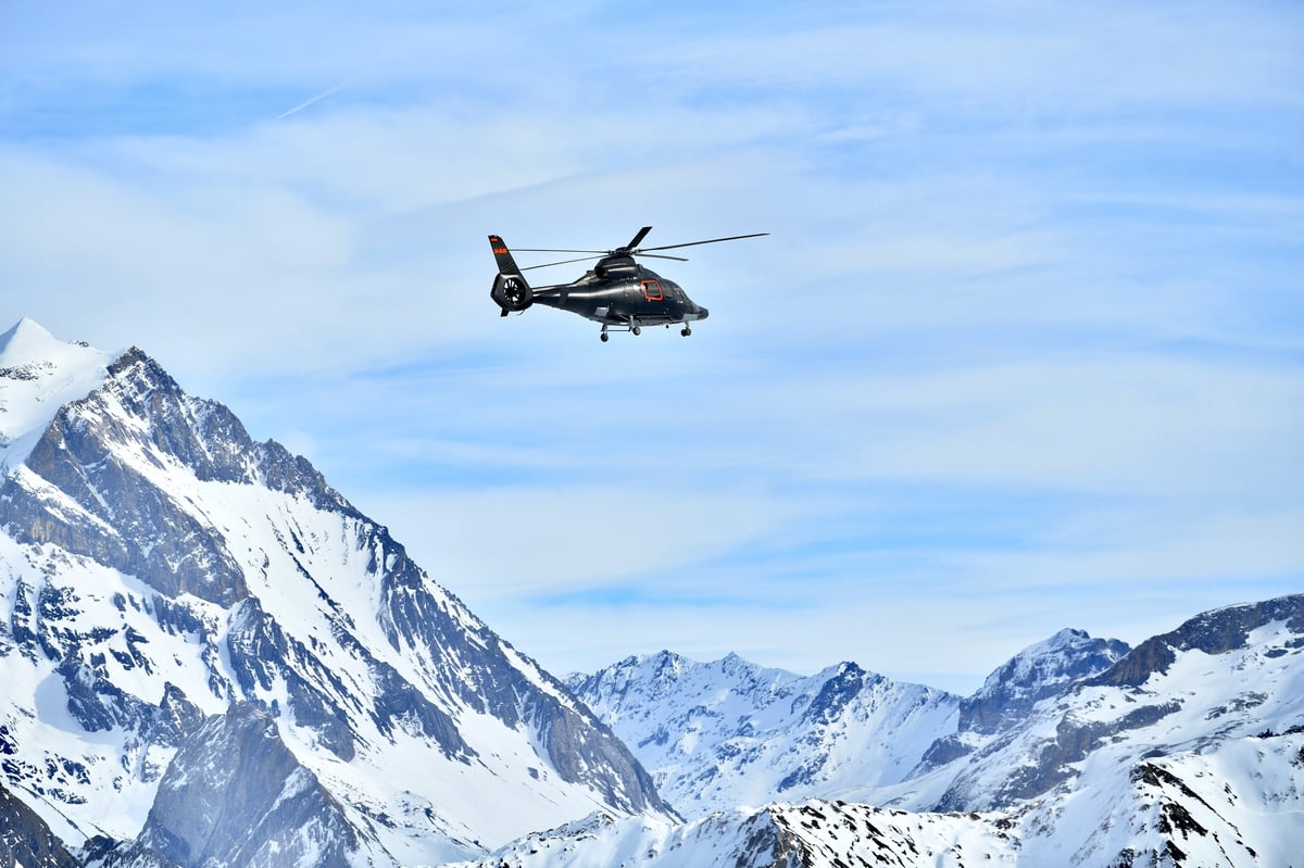 Helicopter flying over steep snow-covered peaks for heliskiing expedition