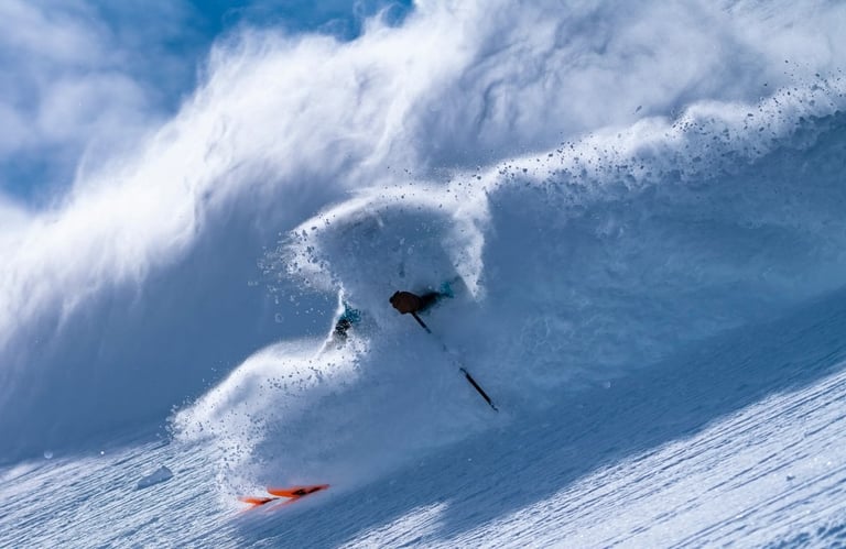 Skier wipes out on massive ocean wave with white spray and blue sky, skis flying in the air