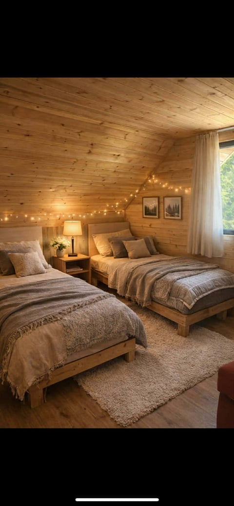 Cozy wooden cabin bedroom with two beds, warm string lights, bedside lamp, and framed forest artwork