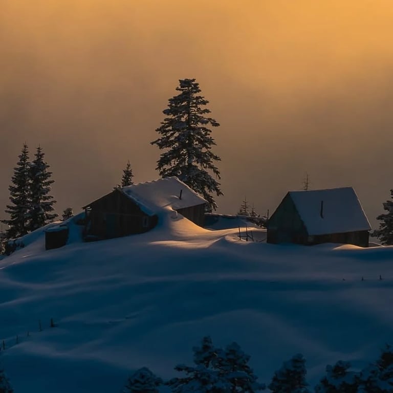 Snow-covered cabins with pine trees at sunset in a winter mountain landscape with golden sky