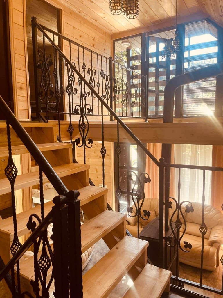 Wooden staircase with ornate black iron railings and balusters in a bright log cabin interior with large windows